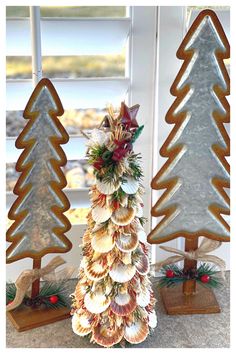 three christmas trees made out of seashells on display in front of a window