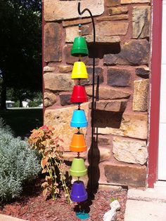 a multicolored lamp is hanging on the side of a brick wall next to a flower bed