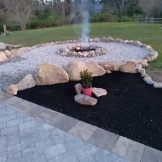 a fire pit surrounded by rocks and gravel in the middle of a yard with a potted plant next to it