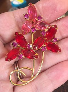 "This is a beautiful red and pink stone flower brooch. Two red flowers on the bottom with one pink on the top. The small accent stone surrounding each of the flowers are pink. Such a lovely yet modern design with the gold tone setting and stem. This brooch measures 2 3/4\" by 1 3/4\". A total of 18 stones, 9 are marquis cut the other nine are small round stones but look square because they are in a square setting. This piece weighs .6 of an ounce. The shipping weight will be 2 ounces." Pink Ruby Flower-shaped Jewelry, Red Brooch Jewelry For Valentine's Day, Red Brooches For Valentine's Day, Red Valentine's Day Brooch, Red Brooch For Anniversary On Valentine's Day, Red Brooches For Anniversary And Valentine's Day, Black Bead Necklace, Seed Pearl, Pink Stone