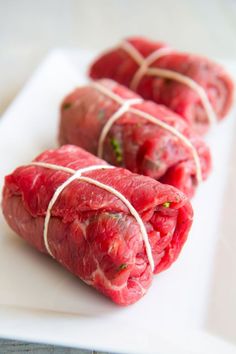 four pieces of raw meat tied together on a white plate with green garnish