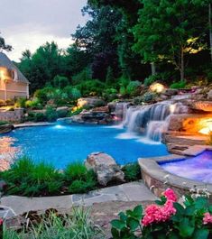 an outdoor swimming pool surrounded by landscaping and lights at dusk with waterfall in the background