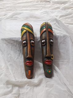 two african masks sitting on top of a white sheet