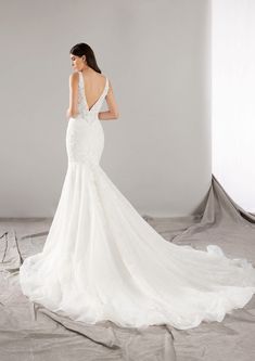 a woman in a white wedding dress is standing on a gray background with her back turned to the camera