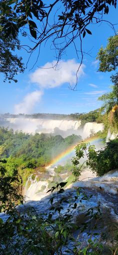 a rainbow shines in the sky over a waterfall with trees and water on either side