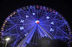 a ferris wheel lit up at night with lights on it's sides and trees in the background