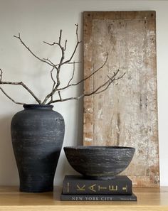 a black vase sitting on top of a wooden table next to a bowl and book