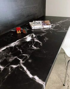 a black marble table with white chairs and books on it in front of a wall