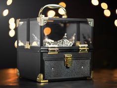 an open black box with gold handles sitting on top of a wooden table next to lights