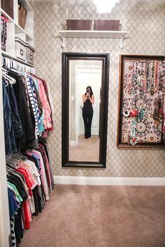 a woman taking a selfie in front of a mirror with clothes hanging on the wall