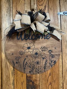 a welcome sign hanging on the side of a wooden door with flowers painted on it