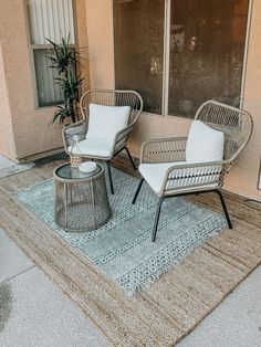 two wicker chairs and a coffee table on a rug in front of a building