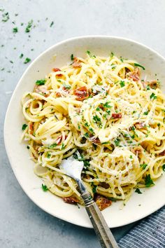 a white bowl filled with pasta and topped with parmesan cheese, bacon and parsley