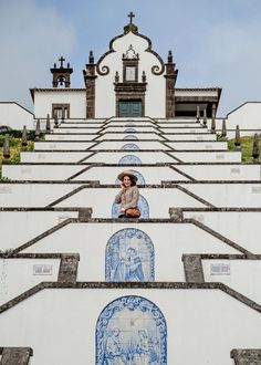 a woman sitting on top of a white building with blue and white tiles in front of her