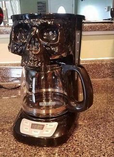 a glass coffee maker with a skull face on the front and bottom, sitting on top of a granite countertop