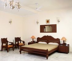 a bed room with a neatly made bed next to two chairs and a mirror on the wall