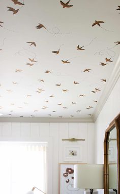 a living room with white walls and birds painted on the ceiling, along with a large mirror