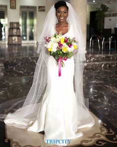 a woman in a white wedding dress holding a bouquet of flowers and posing for the camera