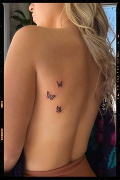 the back of a woman's body with three small butterflies on her left side