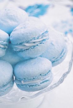 a glass bowl filled with blue macaroons on top of a table