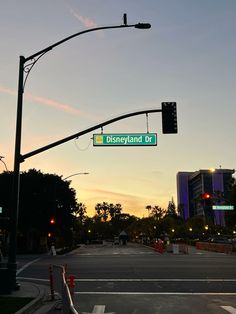 a street sign that reads disneyland dr in front of a cityscape at sunset