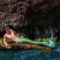 a shirtless man is laying on the rocks next to a body of water with a green mermaid tail