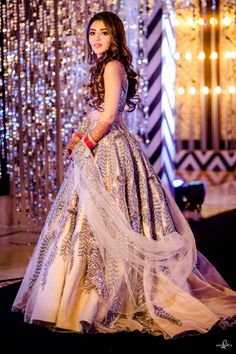 a woman in a white and silver dress standing on a stage with lights behind her