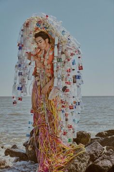 a woman standing on top of a rocky beach next to the ocean covered in plastic bottles