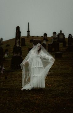 a woman in a white dress and veil walking through a cemetery