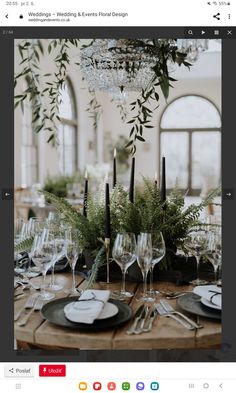 an image of a table setting with wine glasses and place settings on it, surrounded by greenery