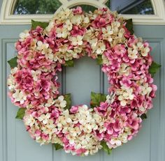 a wreath with pink and white flowers hanging on a door