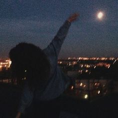 a person reaching up in the air to catch a frisbee at night time