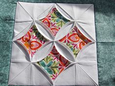 an origami piece is shown on top of a quilted tablecloth with green and orange designs