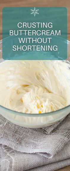 a glass bowl filled with white frosting on top of a wooden table next to a napkin