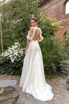 a woman in a white wedding dress standing on a stone path with her back to the camera