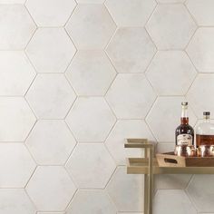 a shelf with bottles and glasses on it in front of a white tiled wall that has hexagonal tiles