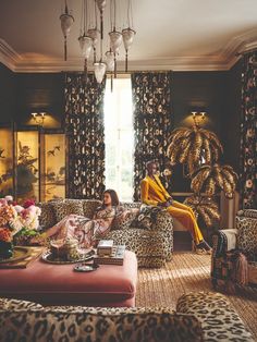 two people sitting on leopard print couches in a living room with chandelier