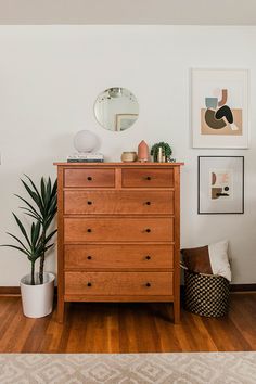 a wooden dresser sitting on top of a hard wood floor next to a potted plant