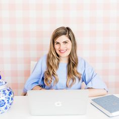 a woman sitting at a table with a laptop in front of her and a teapot behind her