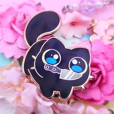 a black cat brooch sitting on top of pink flowers