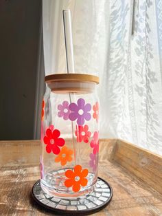 a glass jar with flowers painted on the side and a straw in it sitting on a wooden table