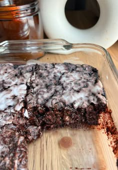 a chocolate cake with white icing sitting in a glass dish on top of a wooden cutting board