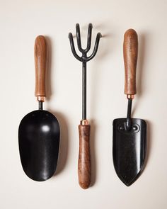 three black and brown garden tools hanging on the wall next to each other with wooden handles