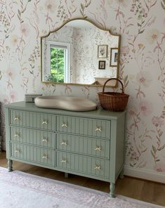 a dresser with drawers and a mirror on it in front of a floral wallpaper