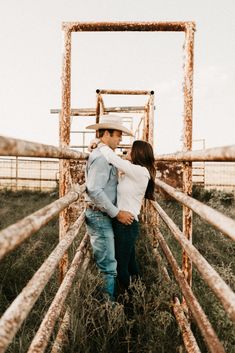 a man and woman standing next to each other in front of a wooden fence with metal bars