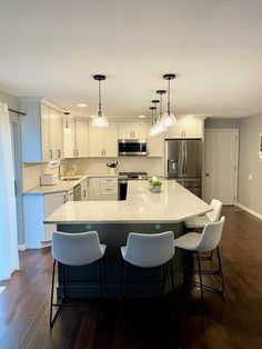 a large kitchen with an island in the middle and white chairs around it, along with stainless steel appliances