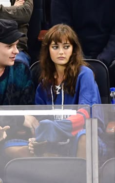 two people sitting next to each other in the stands at a hockey game, one is wearing a beanie