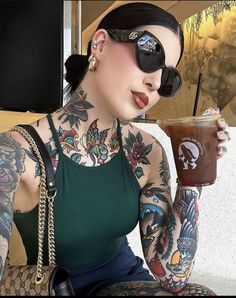 a woman with tattoos holding a drink in her right hand and wearing sunglasses on top of her head