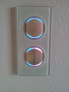 two round lights on a white wall mounted light switch plate with blue and pink lighting