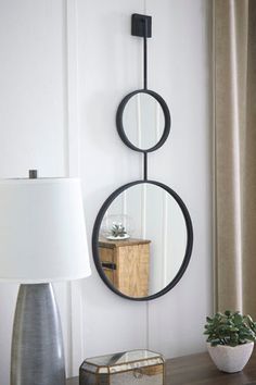 a mirror hanging on the wall next to a table with a lamp and potted plant